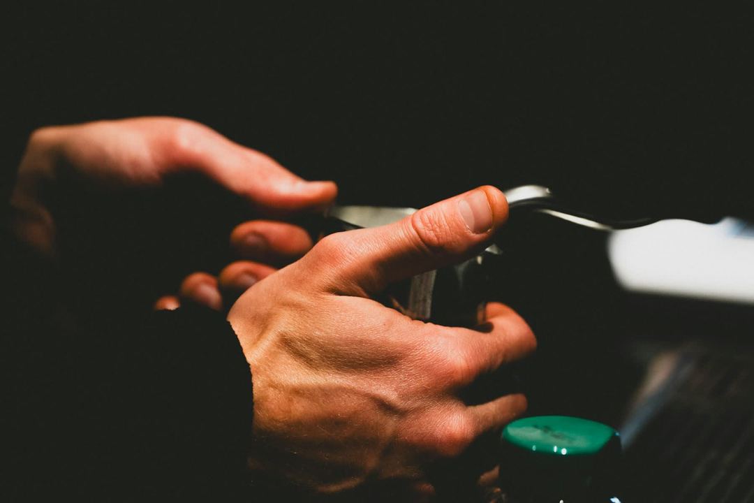 A barista's hands on the portafilter at the machine, a bottle's green cap at the foot of the frame.