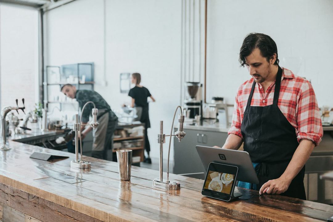 A barista in an apron at a tablet on the counter.